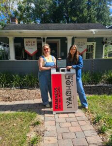 Gold Dust Home Business of the Month photo of owners Shelby, Allie, and the Ivanhoe Village Business of the Month sign in front of the boutique
