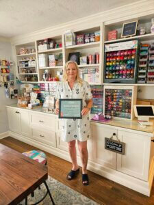 Rene holding a Business of the Month certificate inside of The Craft Table