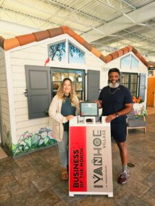 two members of Conduit standing next to tiny house offices and a Business of the Month sign